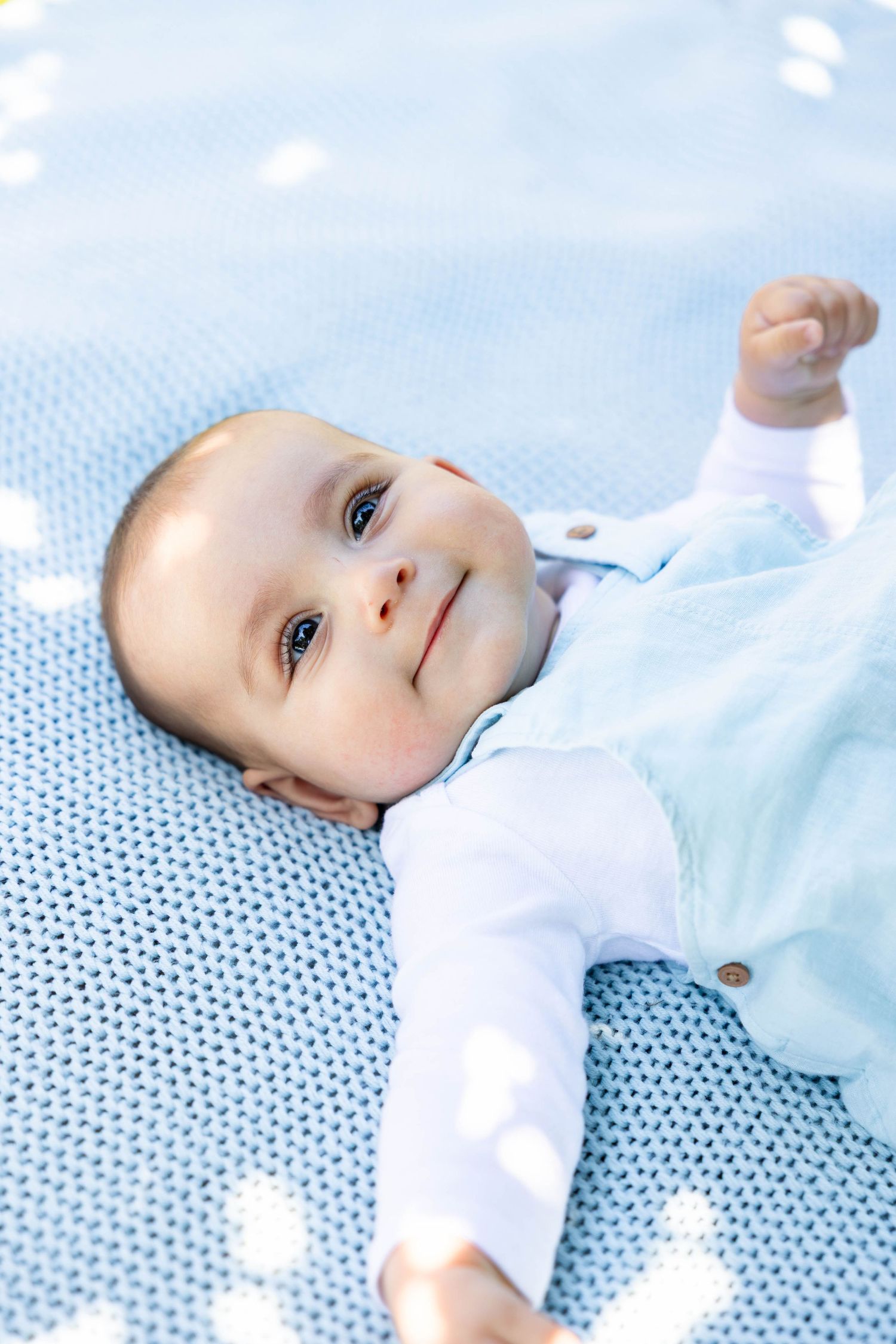 An infant in pastel blue clothing rests on a knitted blue blanket.