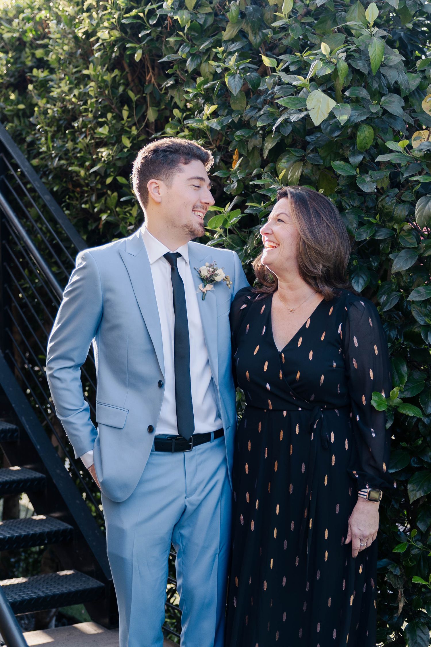 Two people share a joyful moment together outdoors against a leafy green backdrop.
