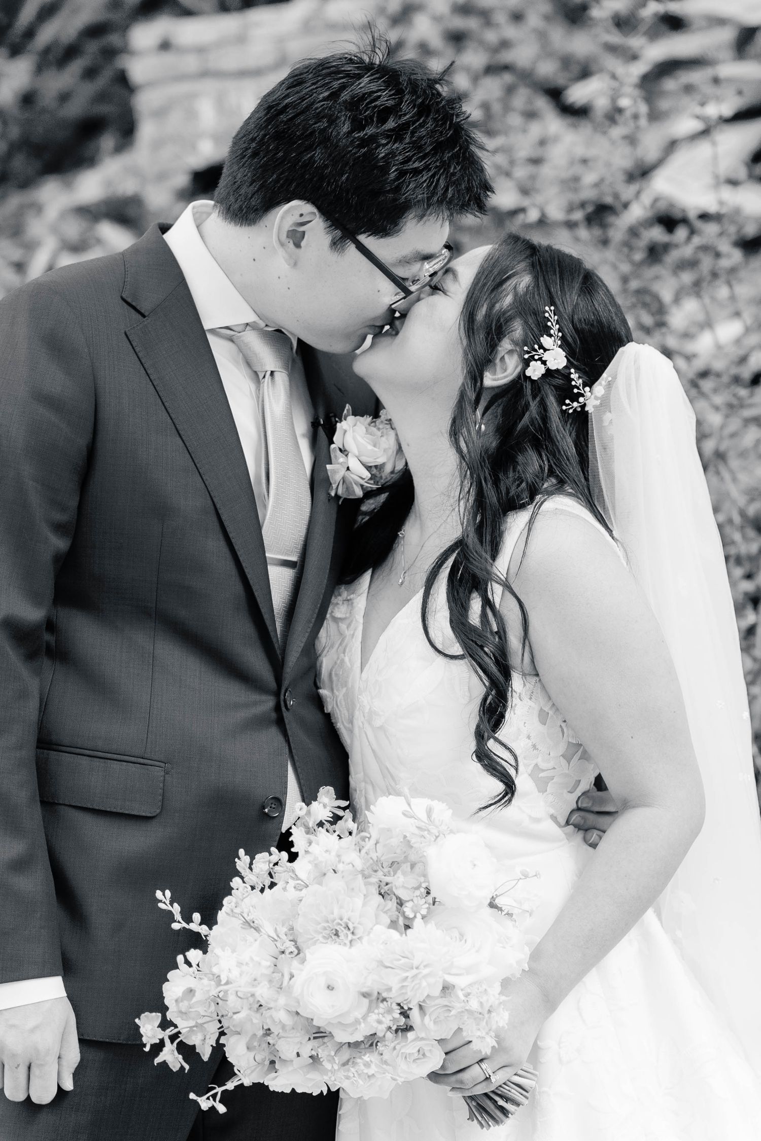 A romantic black and white photo series of a bride and groom sharing tender kisses while holding a white floral bouquet.