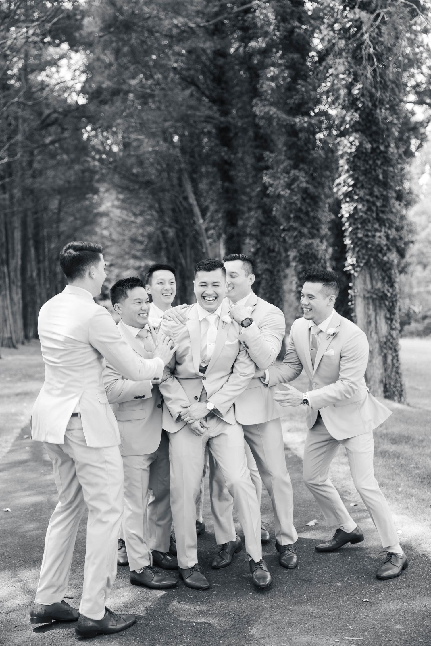 Wedding party members in light suits pose playfully on a forest path.