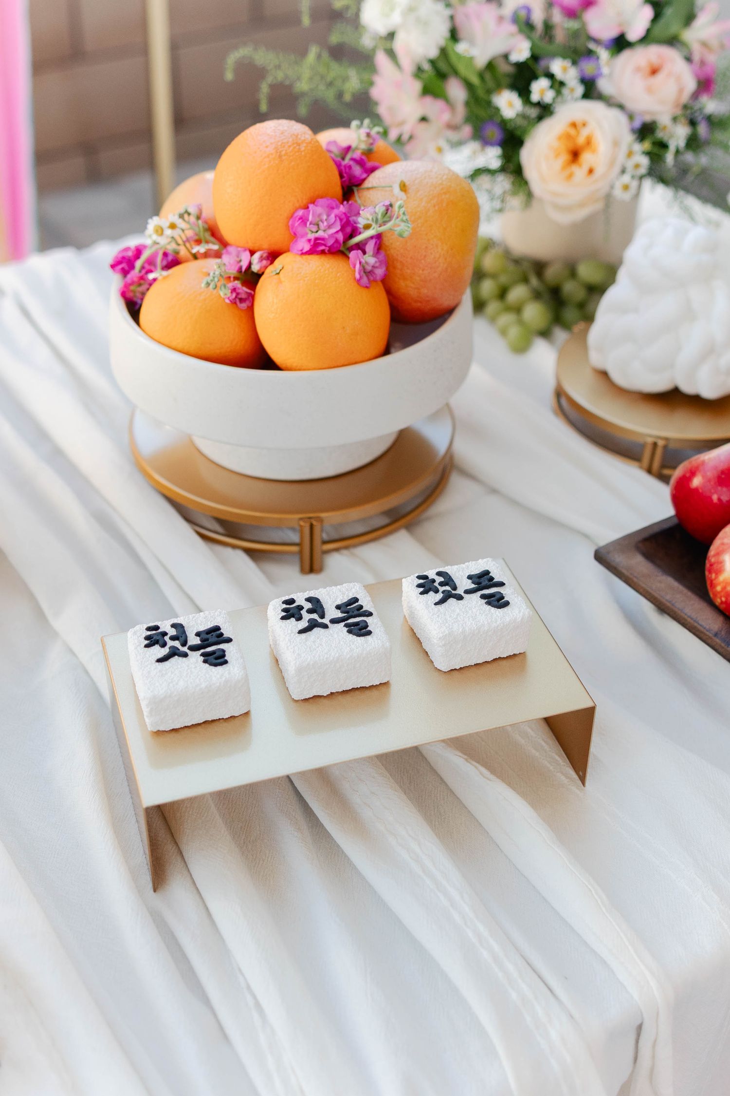 White table setting with fresh oranges in ceramic bowls, floral arrangements, and decorative paper elements.