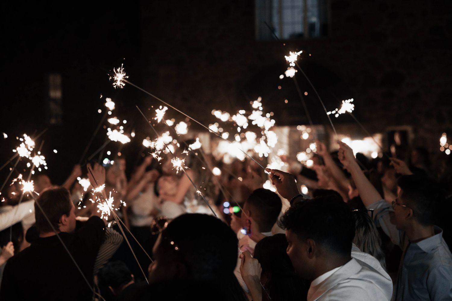 Wedding guests holding sparklers creating a magical nighttime send-off for the newlyweds.