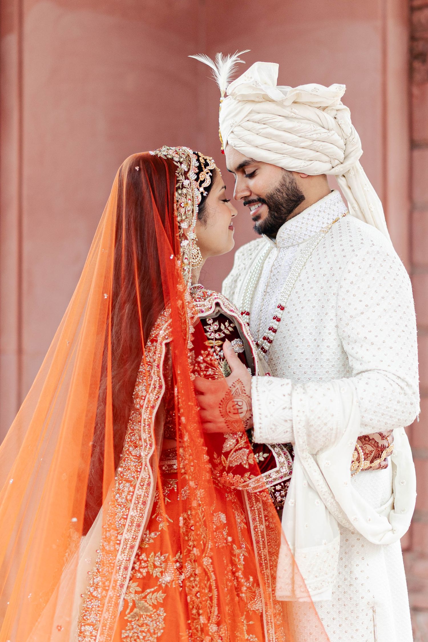 Traditional Indian wedding ceremony showing couple in white and orange attire performing rituals under decorative setting.