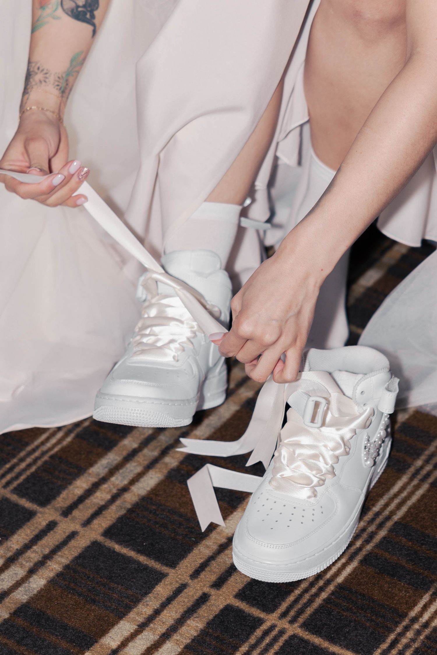 A sequence of photos showing someone tying white laces on white sneakers on a brown and black patterned carpet.