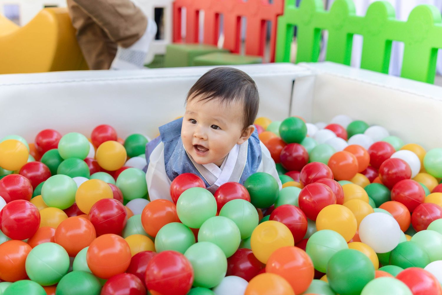 A child plays happily in a colorful ball pit filled with red, green, orange and yellow plastic spheres.