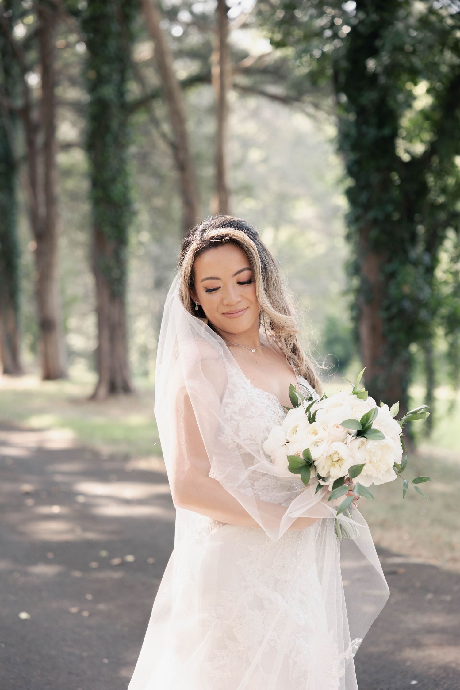 Dreamy forest bridal portrait with white floral bouquet and flowing veil.