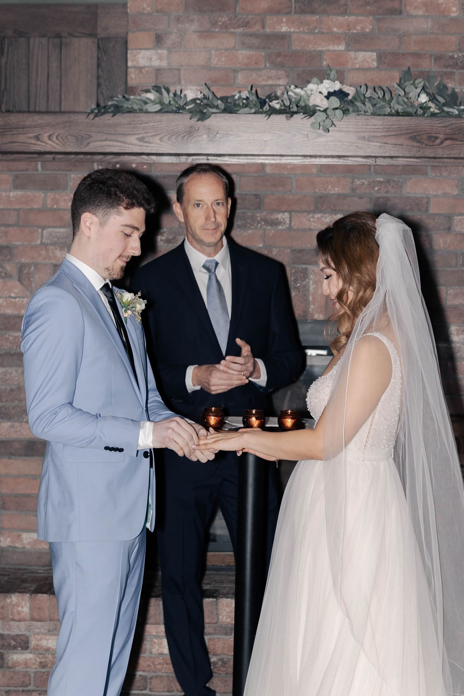 Wedding ceremony moment in a rustic brick-walled venue with decorative greenery.