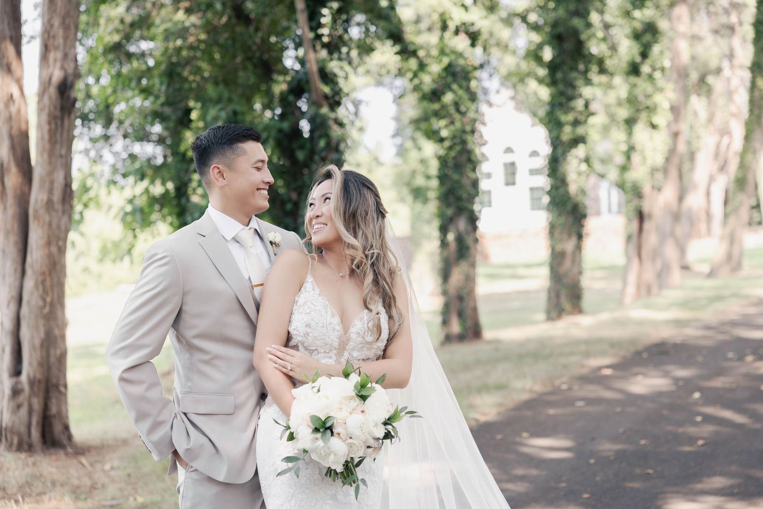Wedding couple posing together on a tree-lined path with natural lighting.