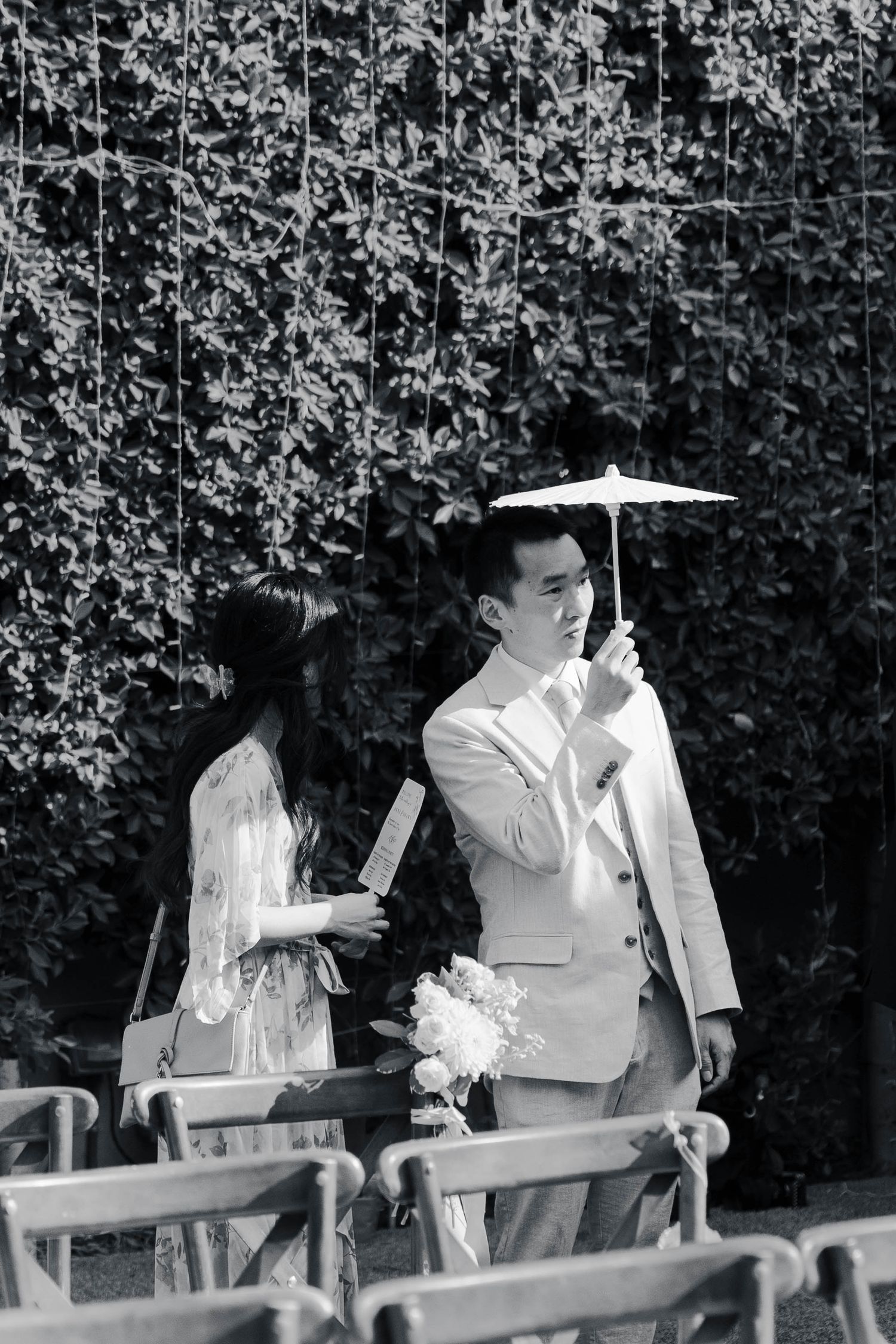 A sequence of black and white photos showing two people in white outfits sitting on a bench in front of a hedge.