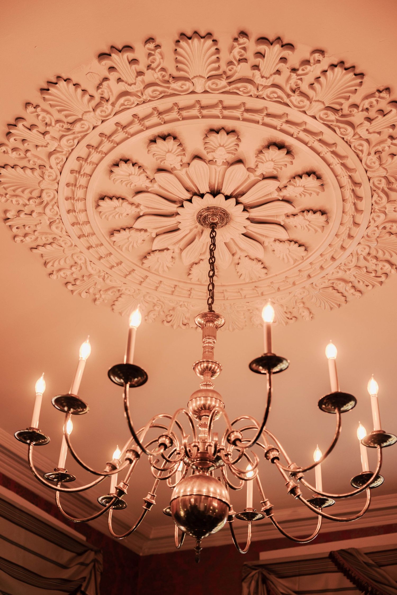 Elegant chandelier with eight candle-style lights hangs beneath an ornate circular ceiling medallion with floral patterns.
