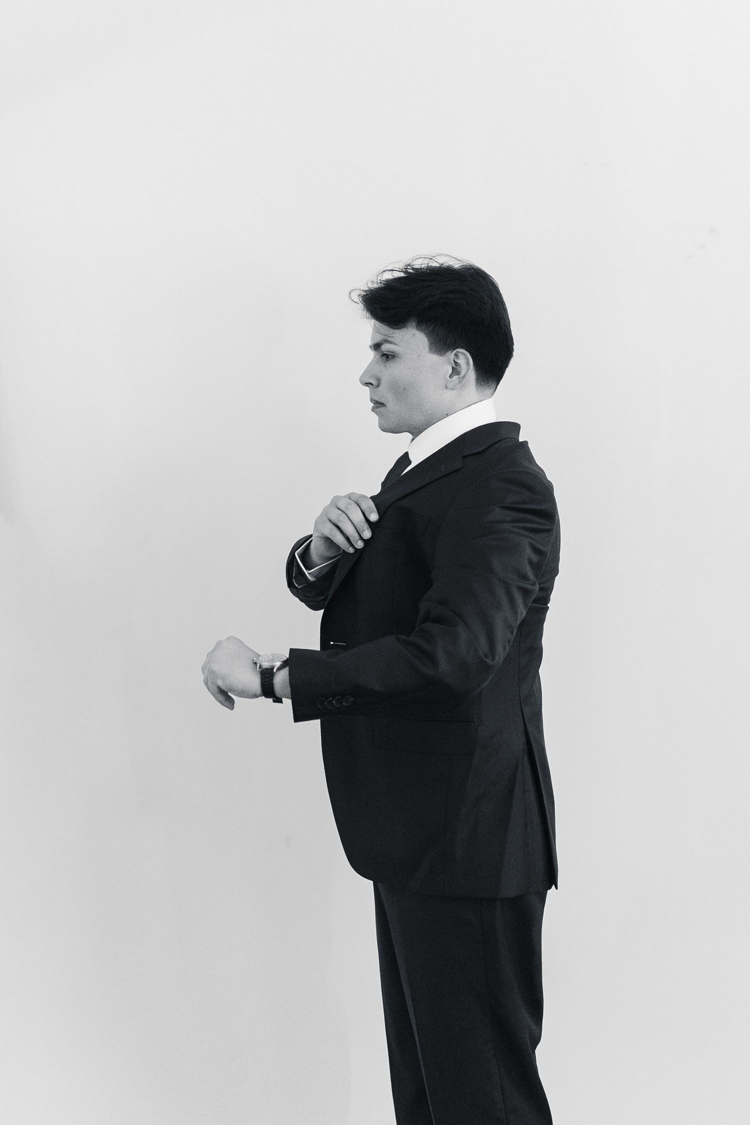 Black and white photo of a young businessman in a suit adjusting his tie, viewed from the side.