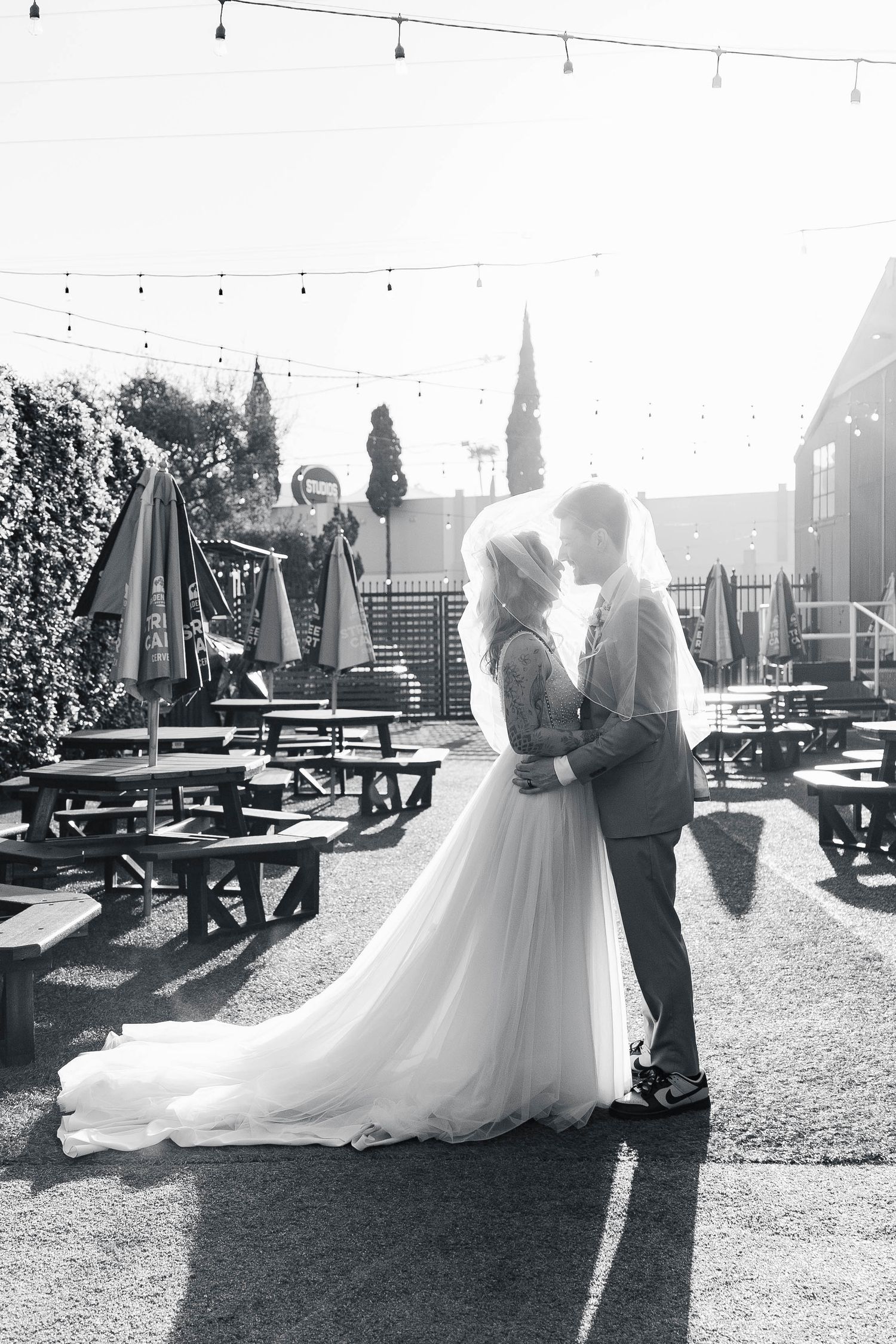 A romantic black and white photo sequence of a couple dancing together in an outdoor garden venue with string lights.