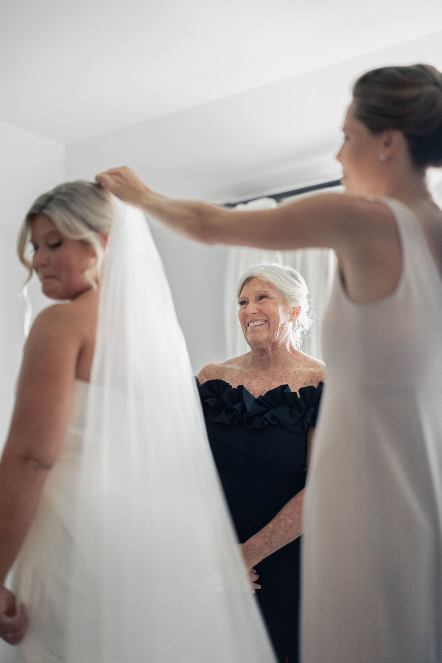 Wedding dress preparations with attendants helping in a bright white room.