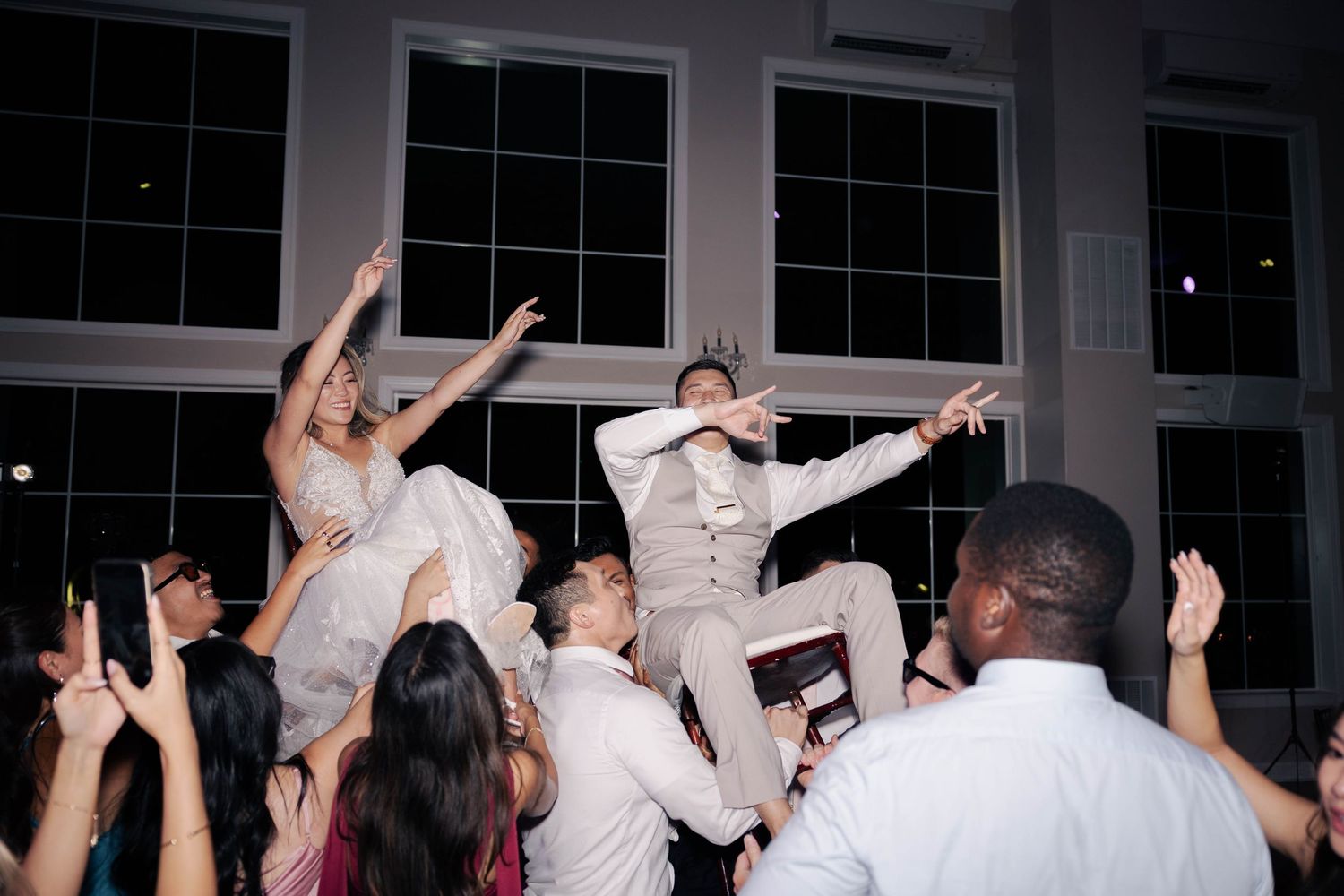 Wedding reception guests dancing with arms raised on a crowded dance floor during evening celebration.