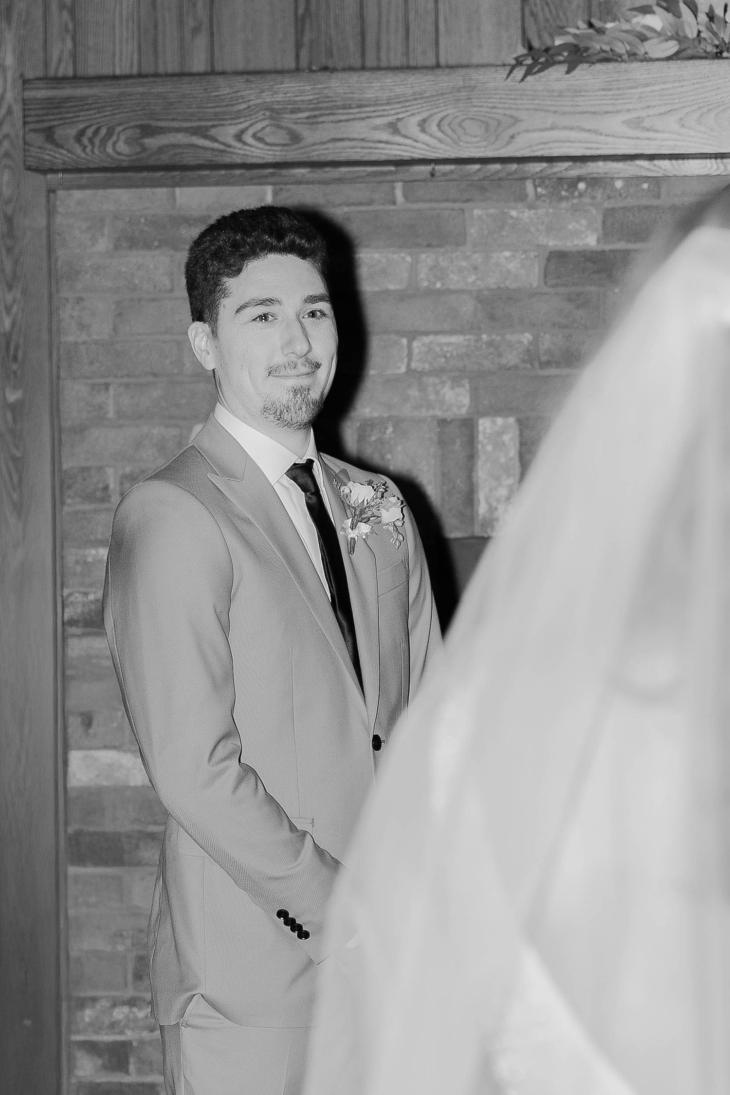 Black and white photo showing a corner of a rustic room with exposed brick and wooden beams.