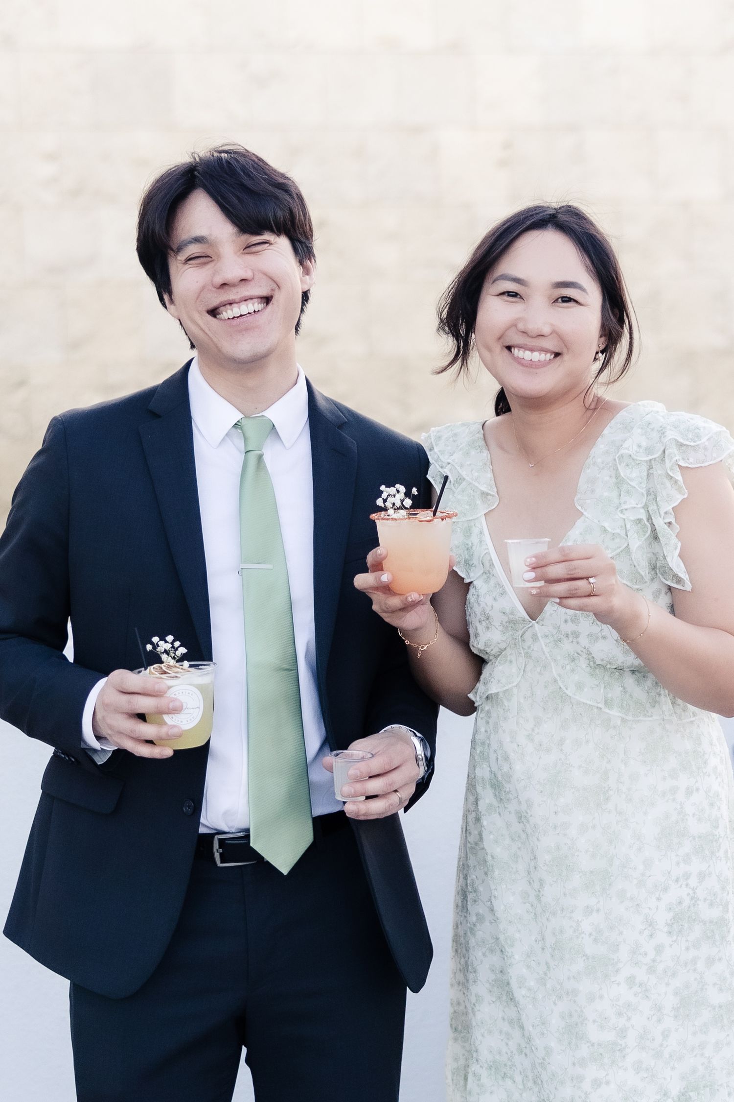 Smiling Asian couple in formal attire holding cocktails at a wedding reception event.