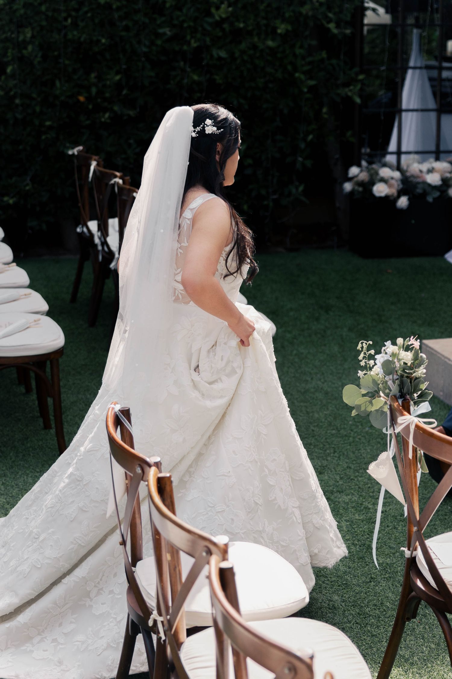 Elegant white wedding dress with lace details draped over a wooden chair on a grassy lawn at an outdoor ceremony.
