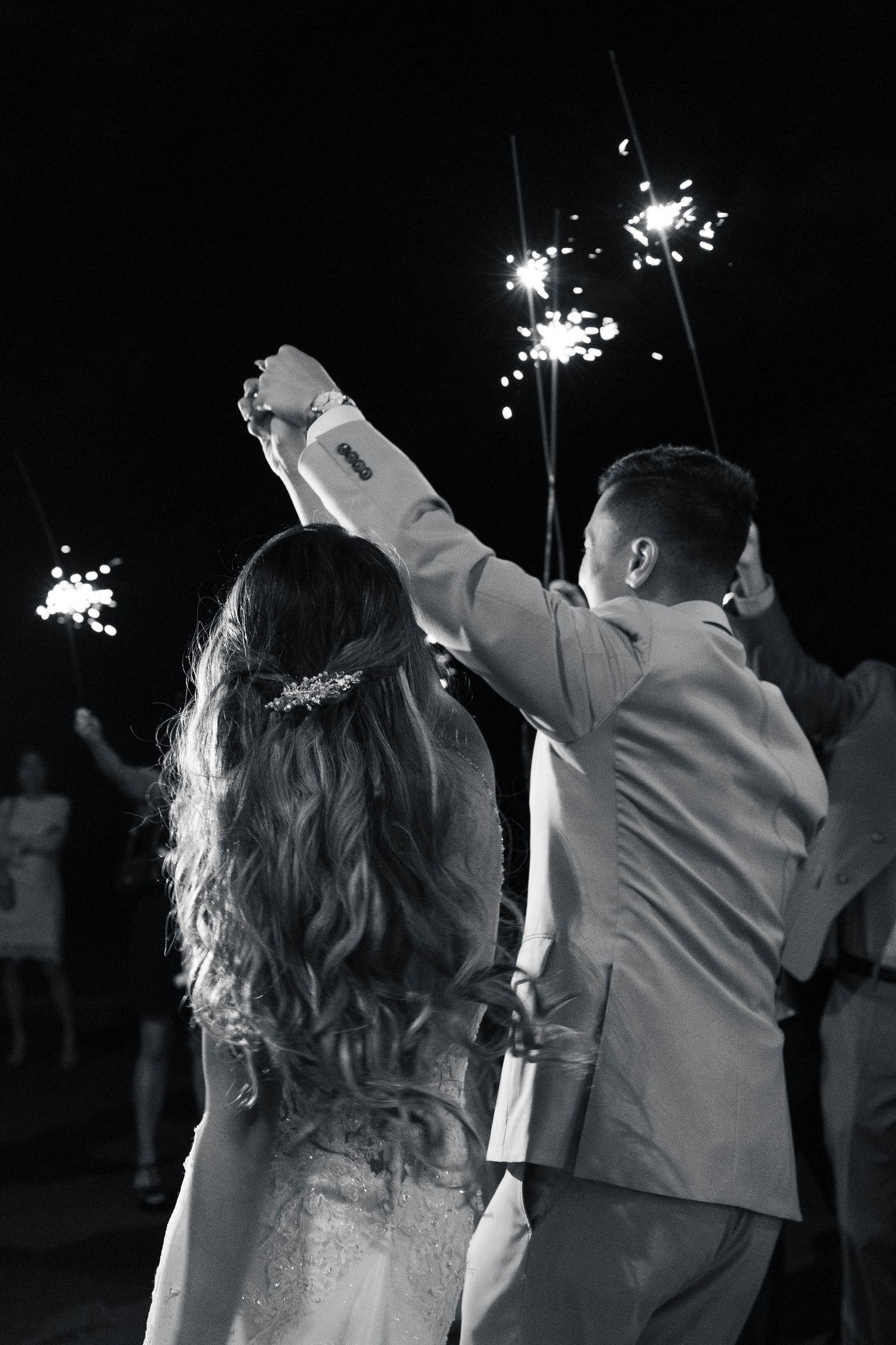 Black and white photo of newlyweds walking through sparklers during their wedding exit.