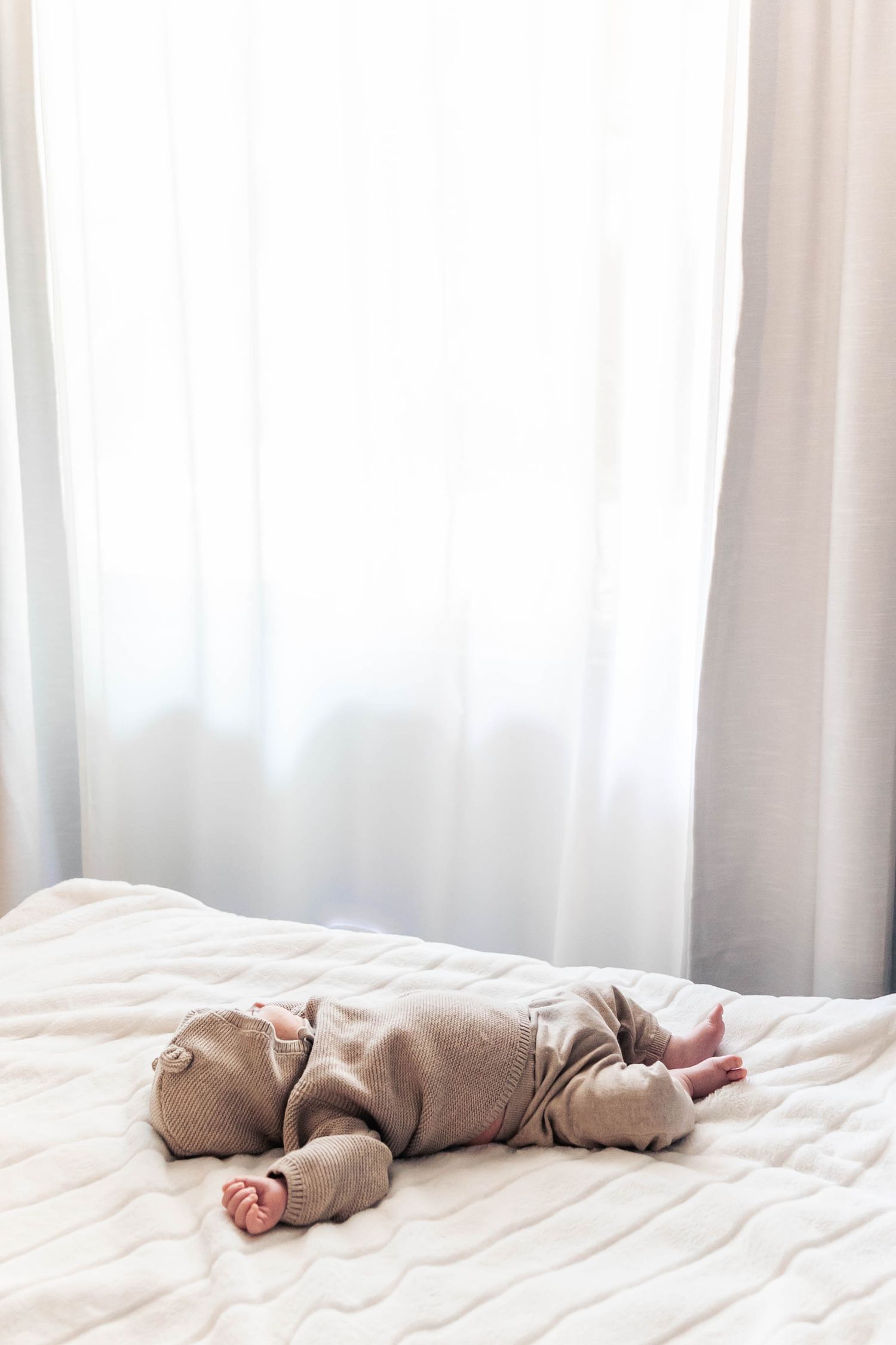 Baby in gray onesie sleeping peacefully on white bedding.