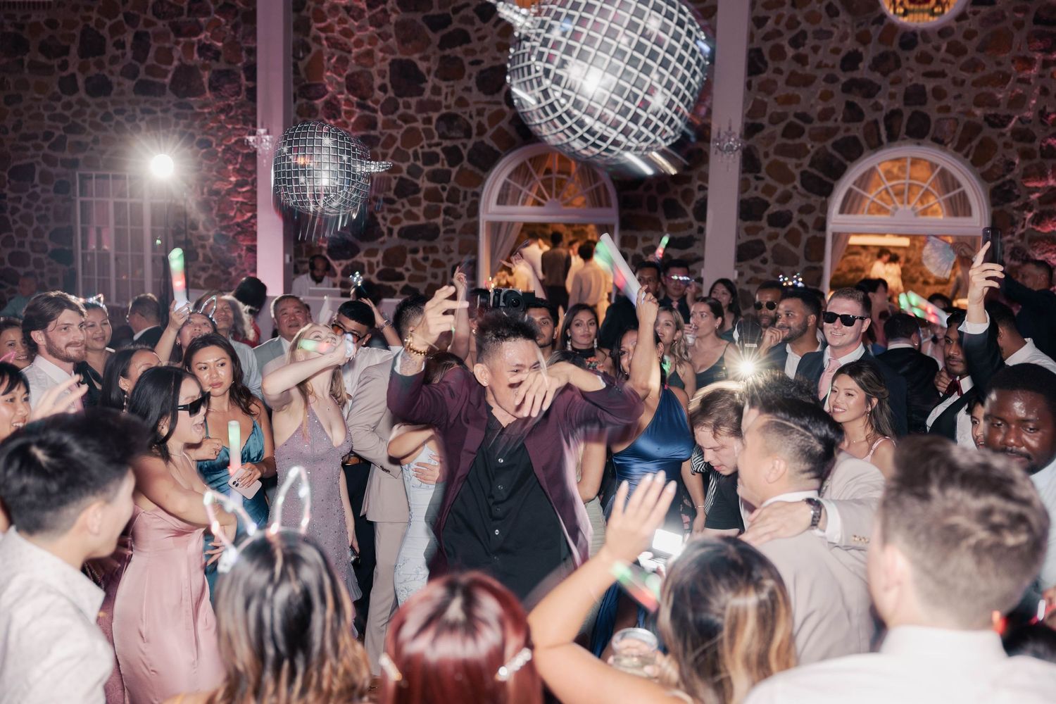 Wedding reception dance floor under disco ball with guests celebrating.