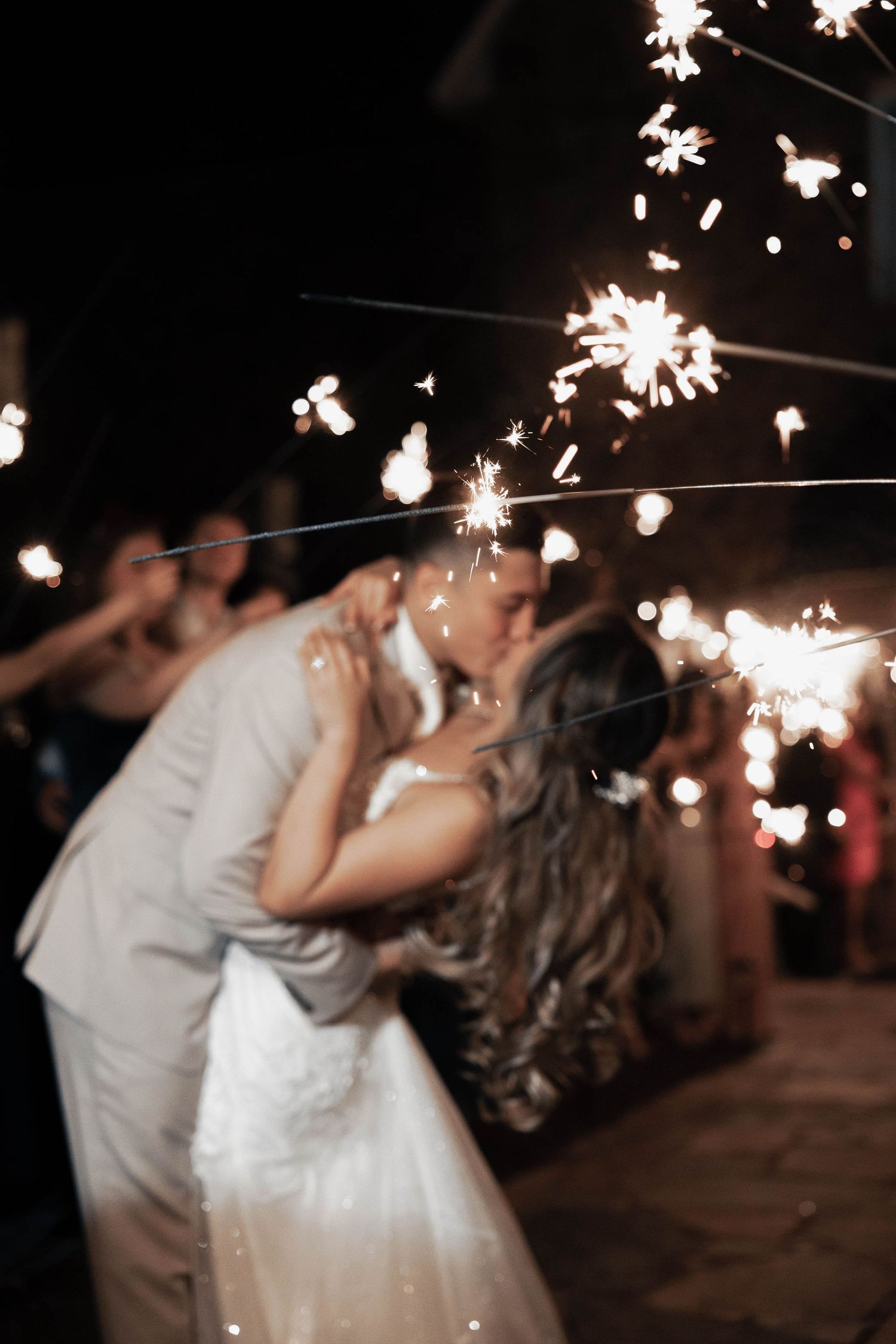 A couple dances and kisses under glowing sparklers at an evening wedding celebration.
