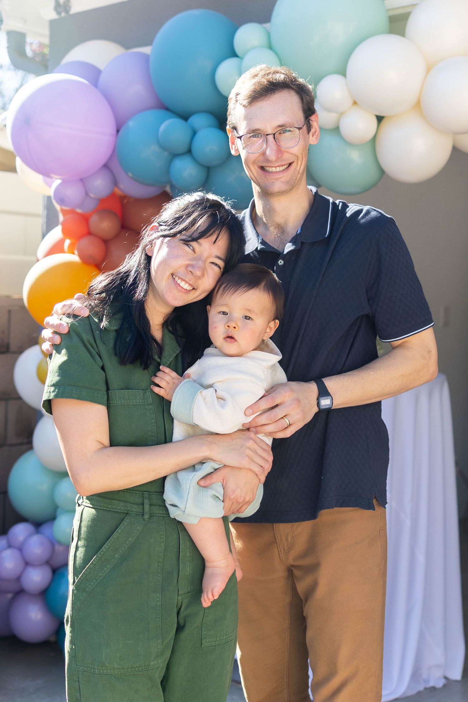 A family poses together against a colorful balloon arch backdrop in a series of four candid photos.
