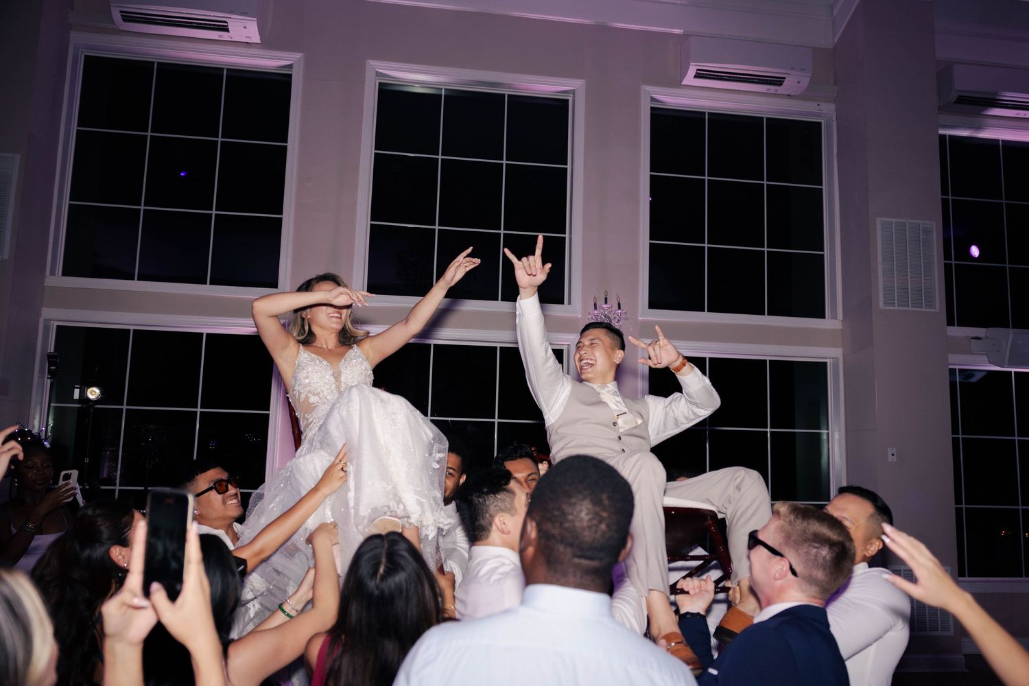 Energetic crowd dancing with hands in the air at a nighttime wedding reception party.