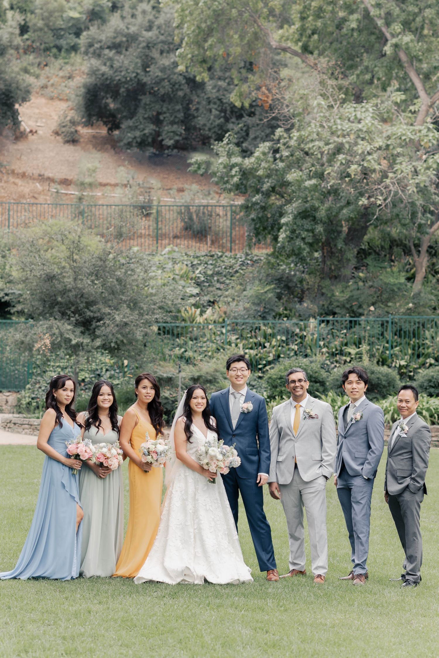 Wedding party in blue, yellow and gray attire posing together on a grassy hillside.