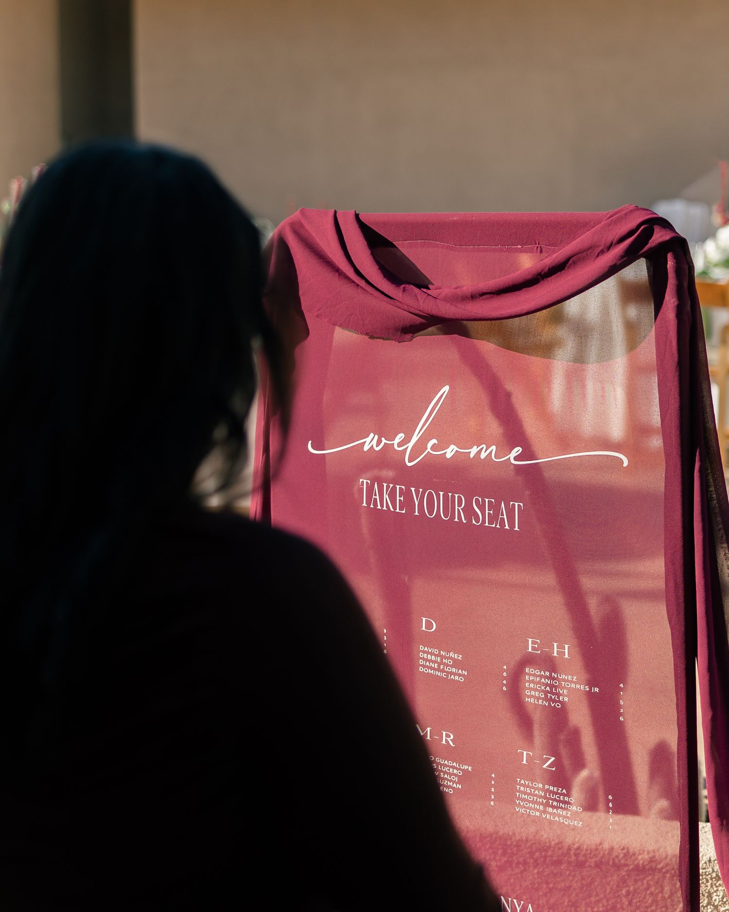 Elegant burgundy wedding seating chart sign with welcome message displayed at a reception venue.