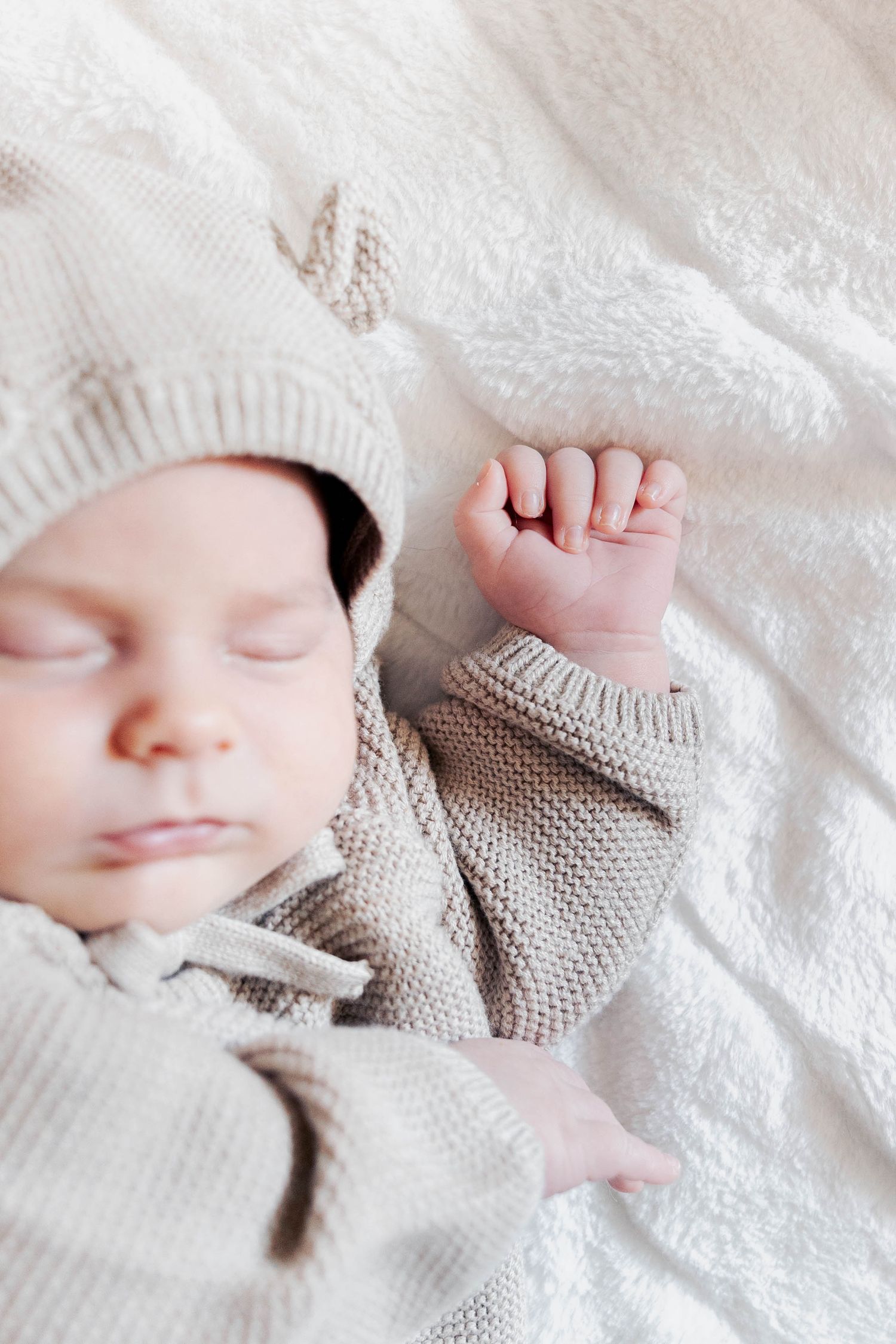 Sweet newborn sleeping peacefully in a gray knit outfit on white lace.