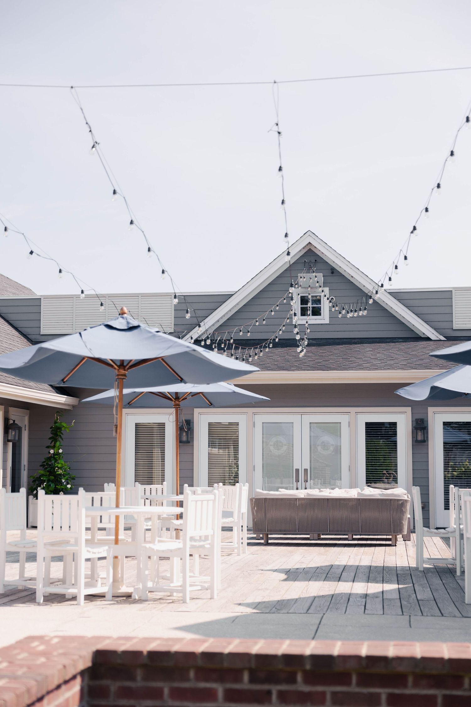 Modern outdoor patio venue with white furniture and string lights under a grey coastal building.