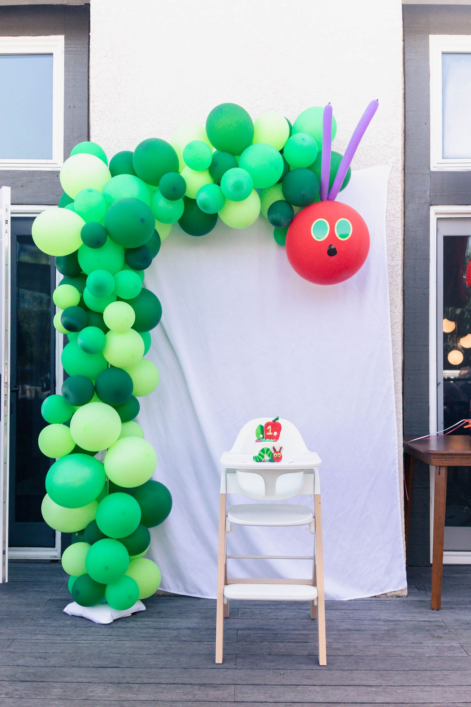 Green and light green balloon arch decorations with small red accents create a festive display against a white backdrop.