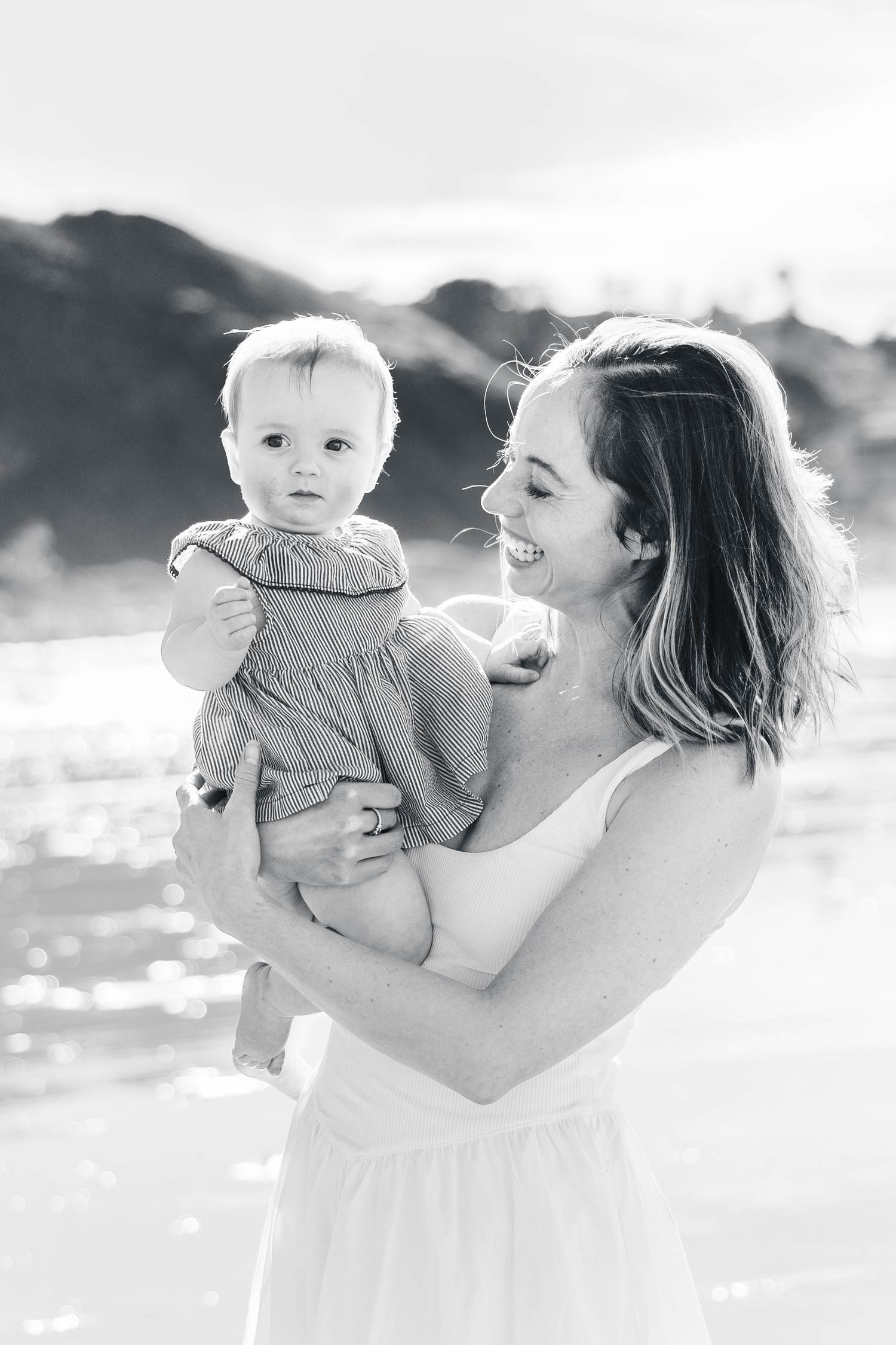 A joyful parent and baby share tender moments together outdoors in black and white photography.