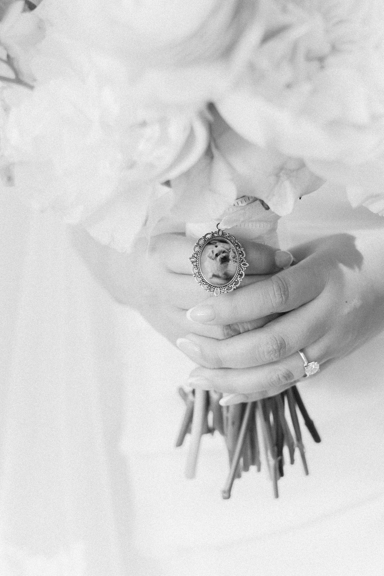 Black and white photo of bride holding floral bouquet with memorial locket charm and diamond engagement ring.