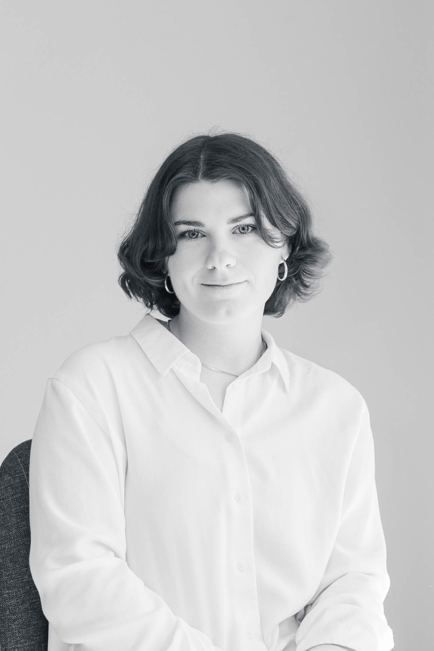 Black and white portrait of a young woman with short dark hair wearing a white button-up shirt, smiling softly.