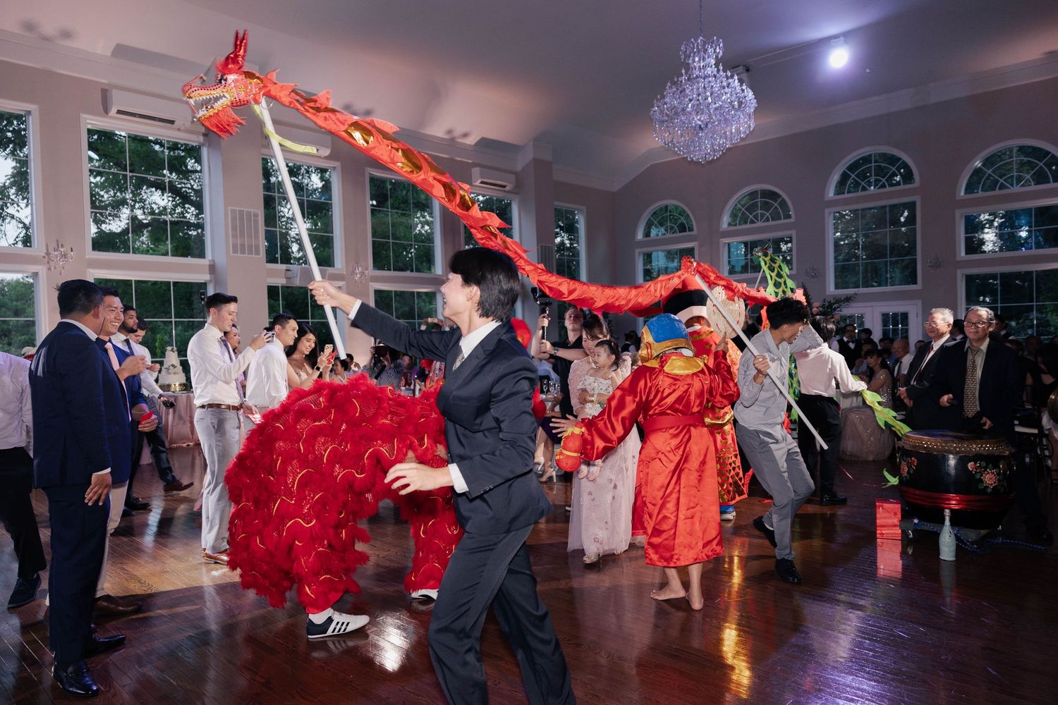 Panoramic view of lion dance performance in elegant wedding reception hall with arched windows.