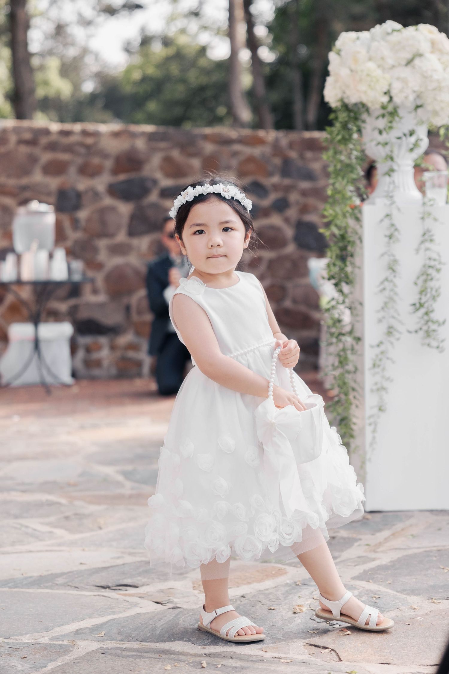 Small child in white lace dress poses on stone steps during a formal occasion.