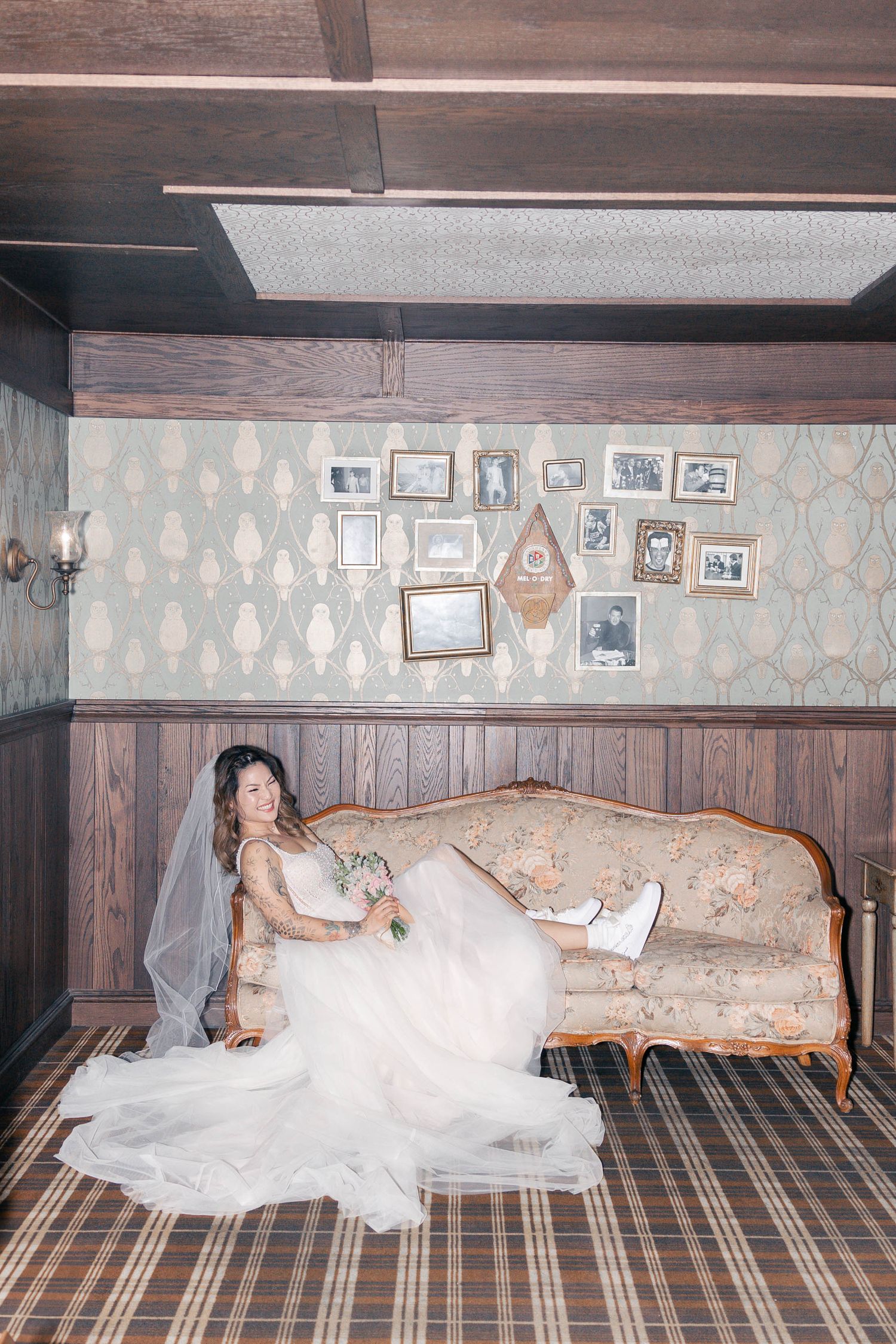 Wedding party lounging on vintage furniture in a room with patterned wallpaper.