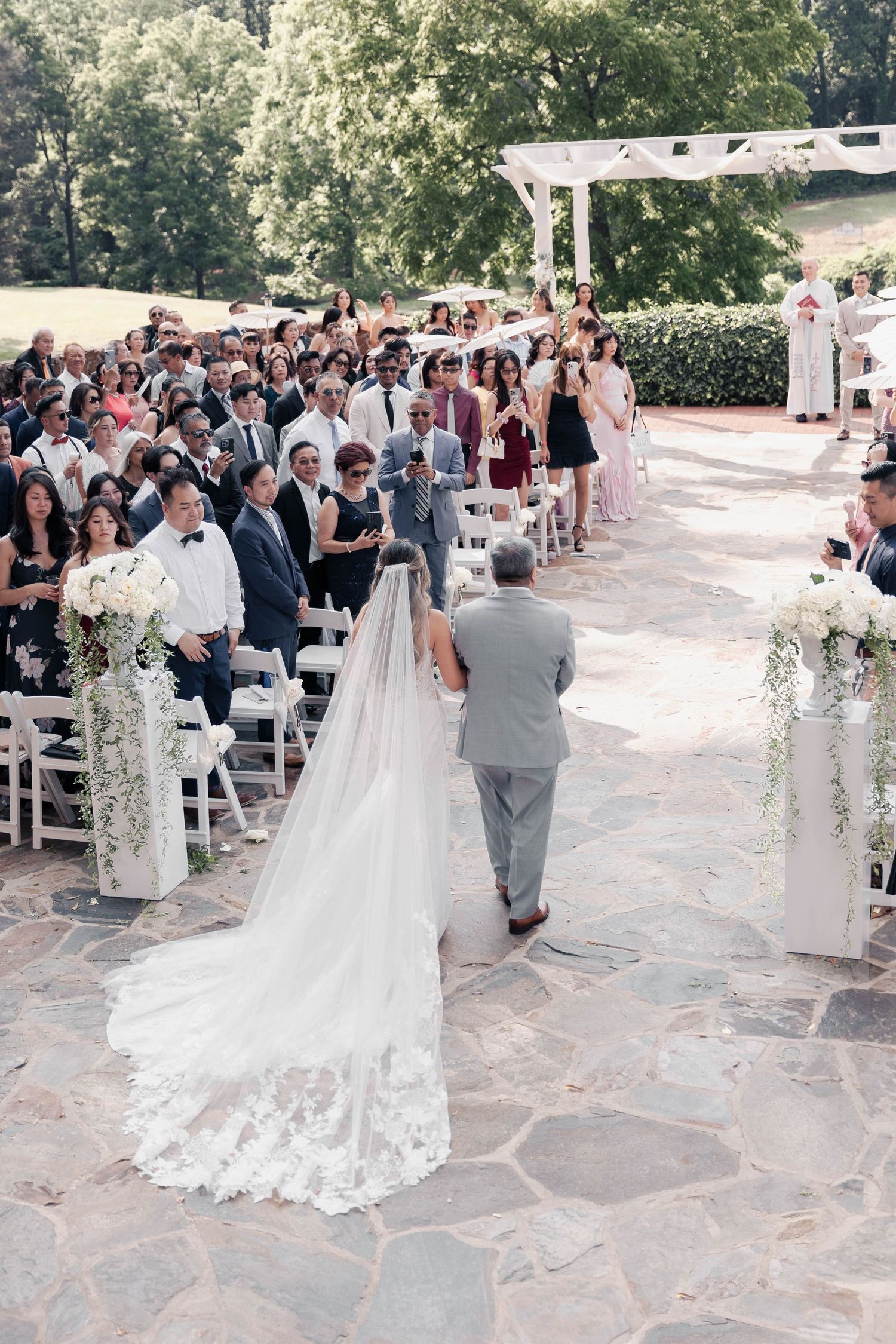 Wedding ceremony on an outdoor stone patio with white floral decorations and seated guests.