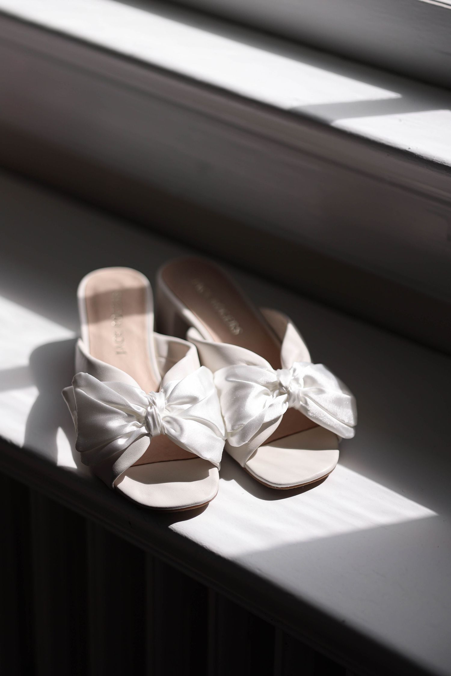 A sequence of white ballet shoes illuminated by dramatic window light on a dark windowsill.