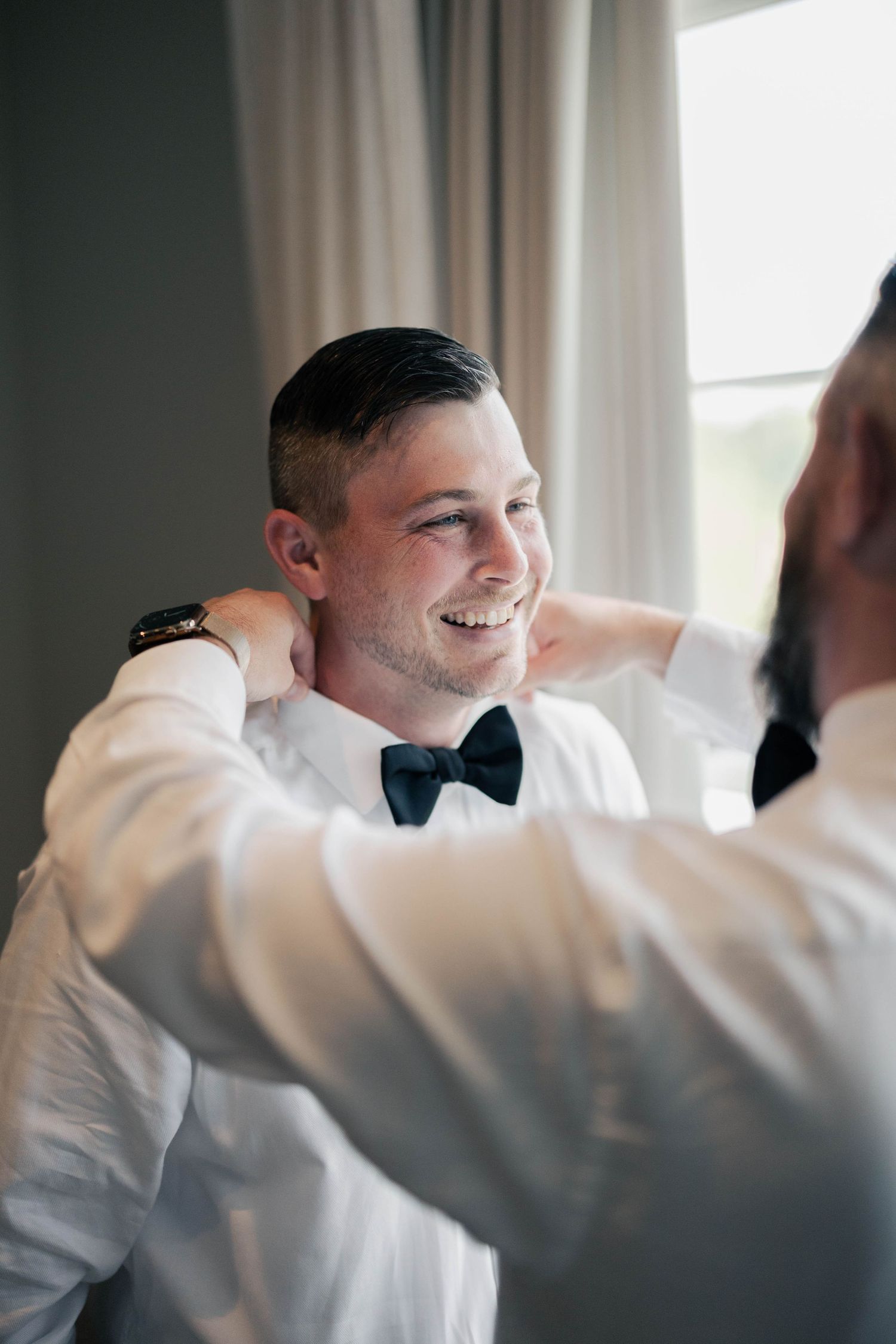 Groom getting ready for wedding while wearing white dress shirt and bow tie.