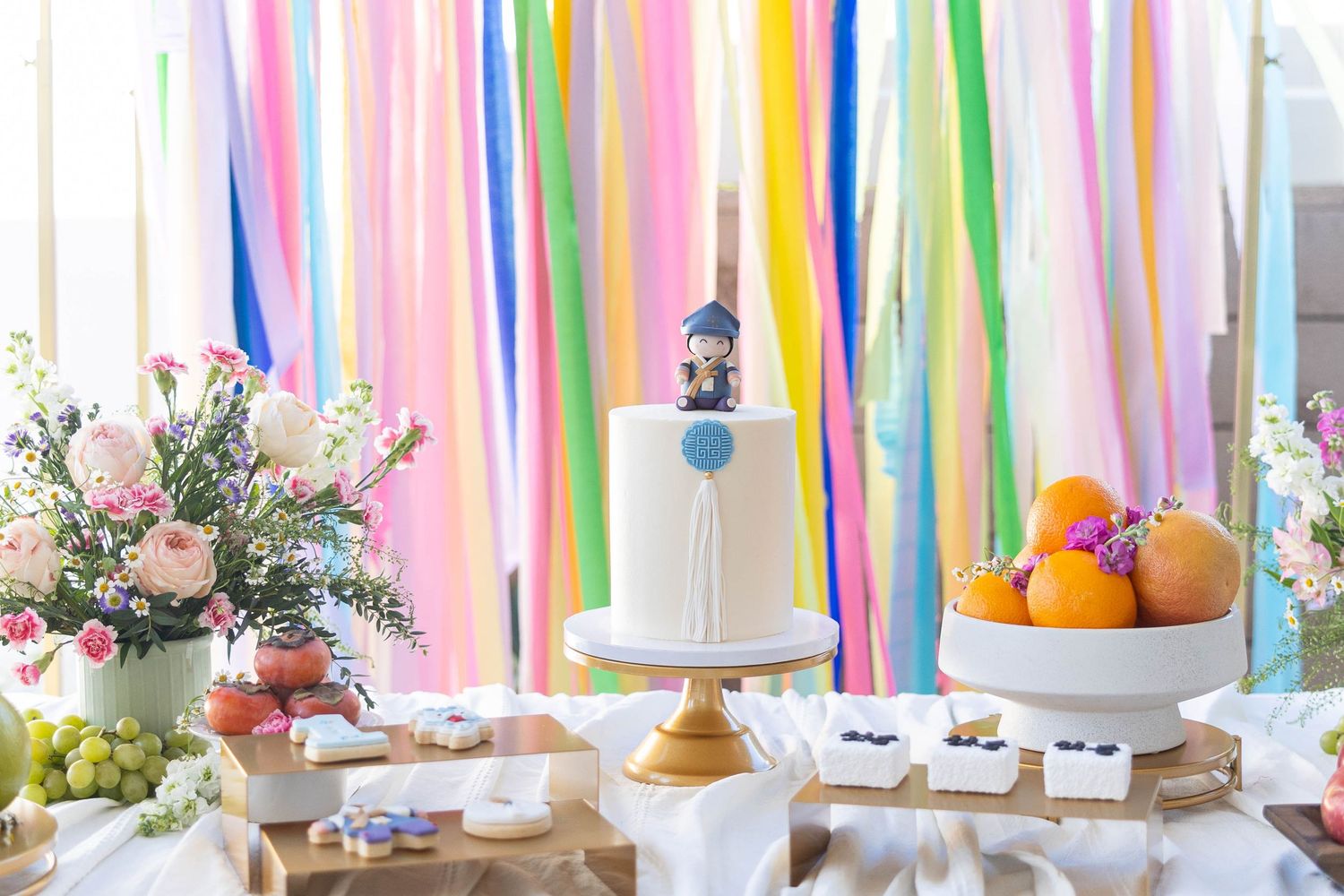 Colorful paper streamers decorate a bright window display with festive party decorations and white cakes.