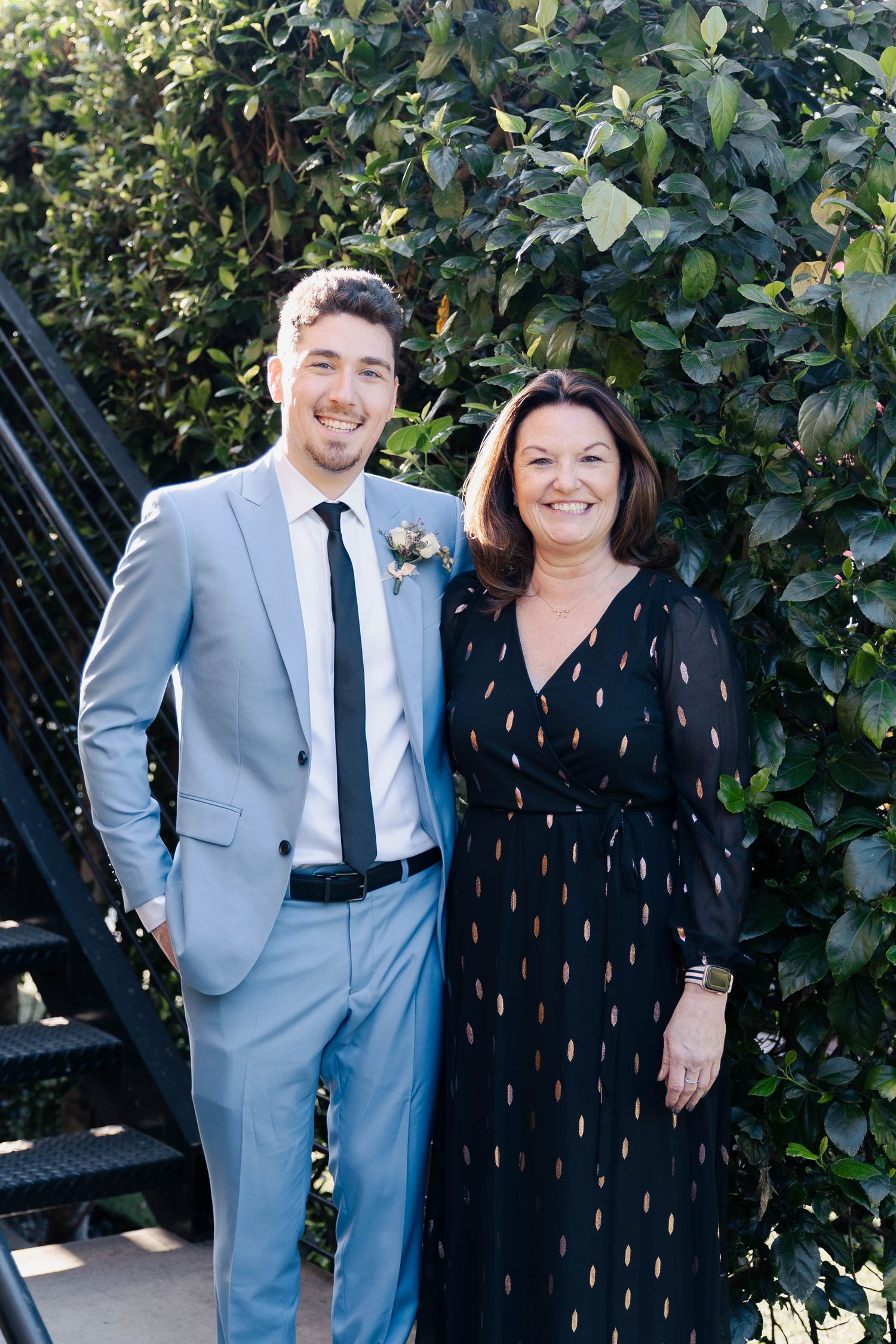 Formal portrait of two people against green foliage backdrop.