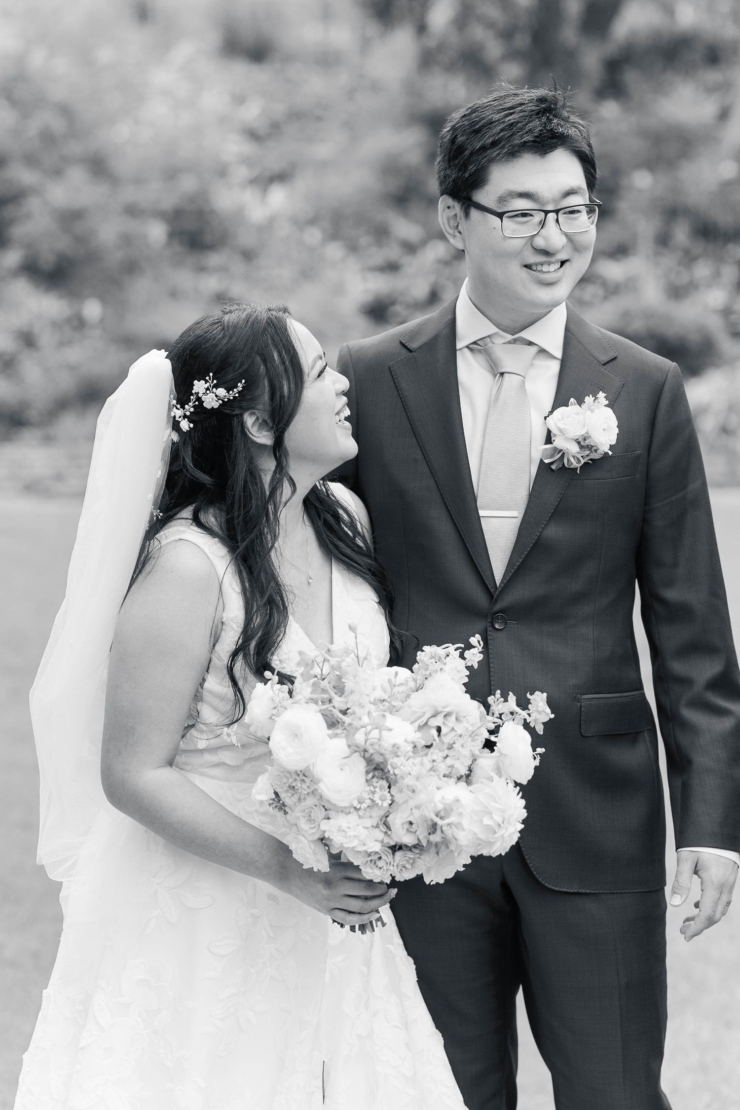 Black and white portrait of a couple in wedding attire holding a bouquet of white flowers.