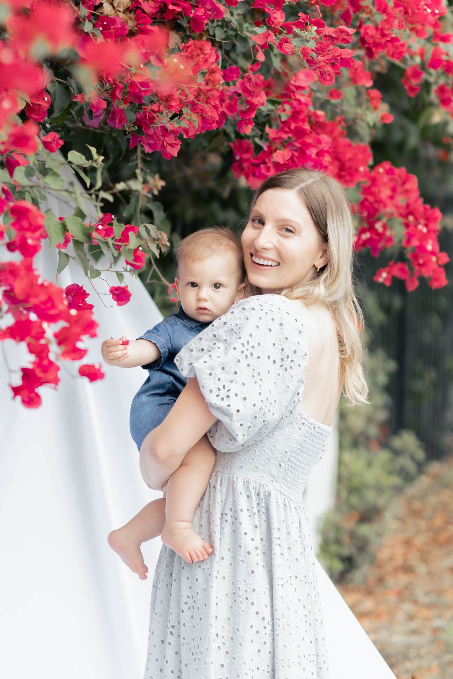 A tender family moment captured against vibrant pink bougainvillea flowers in an outdoor garden setting.