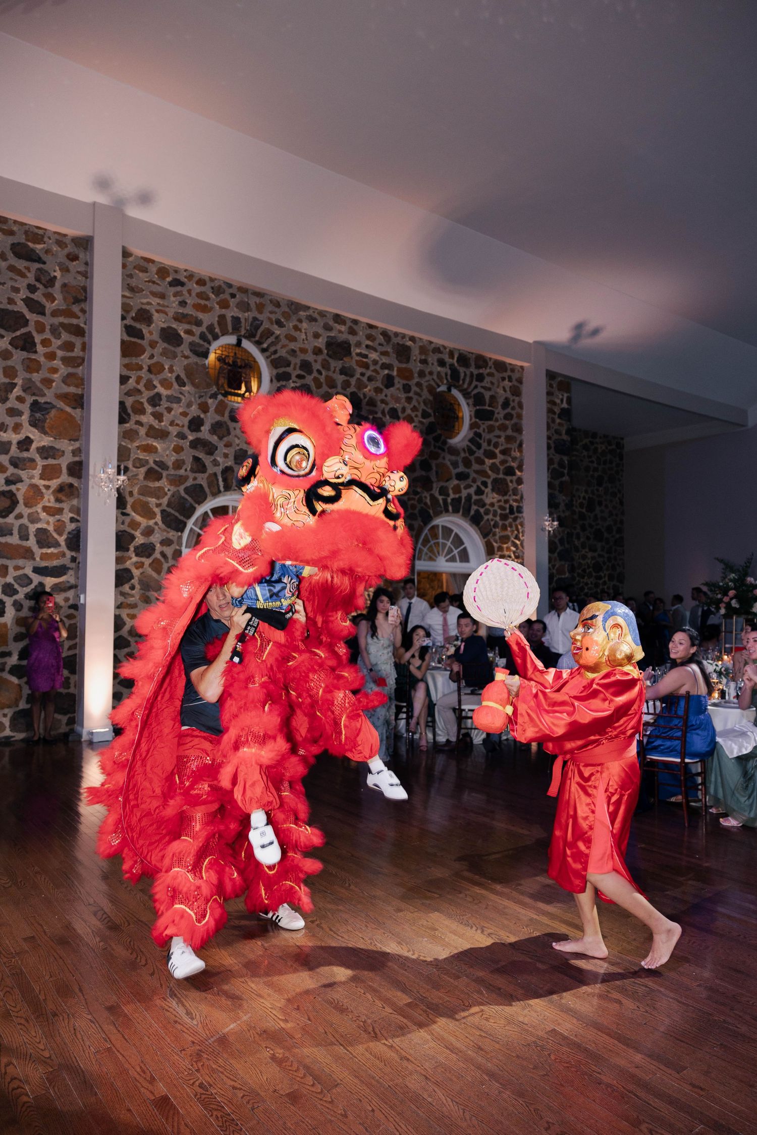 Multiple lion dancers in vibrant red costumes performing coordinated movements at indoor wedding venue.