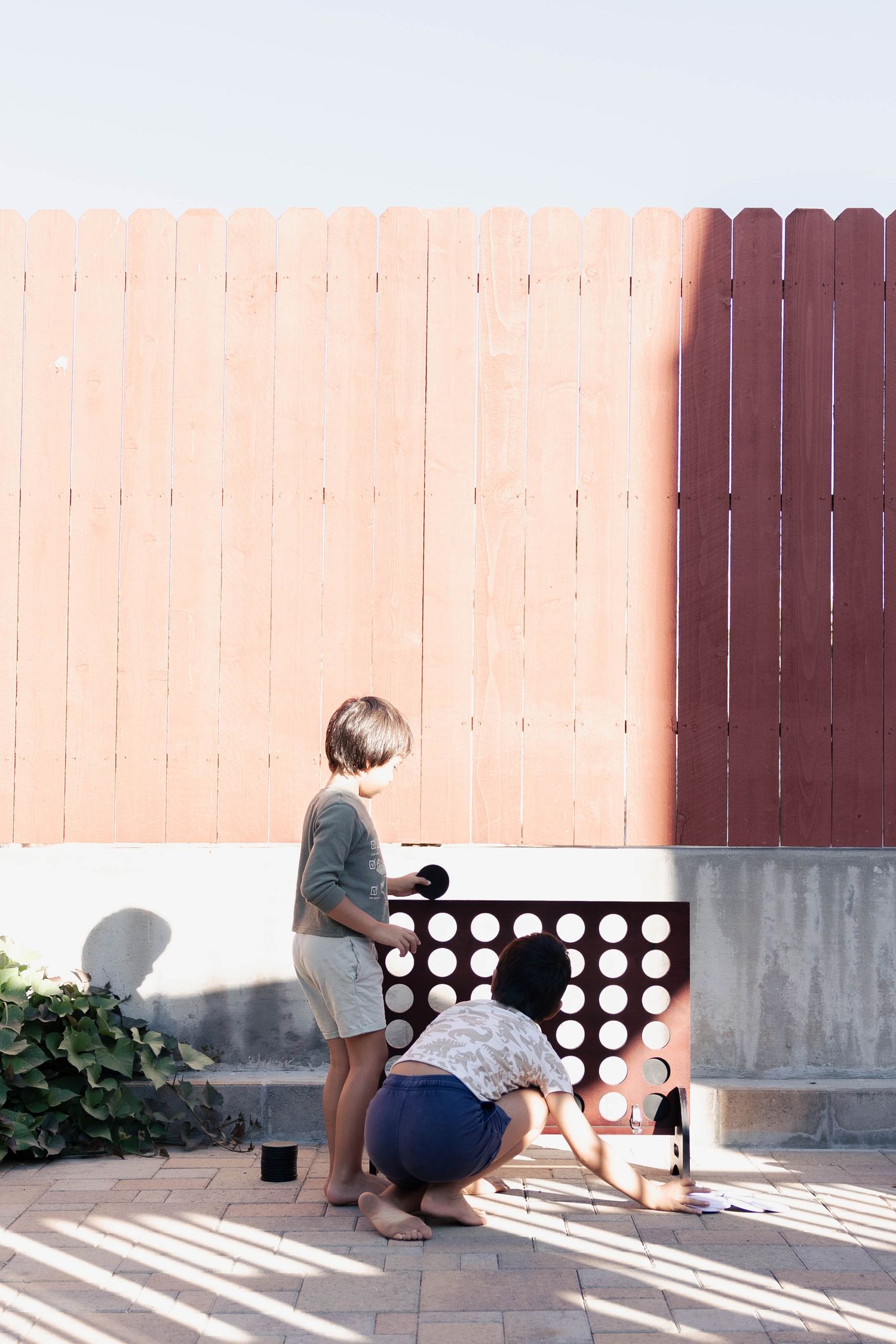 People playing a game of tic-tac-toe with chalk on a concrete patio in sunlight and shadow.