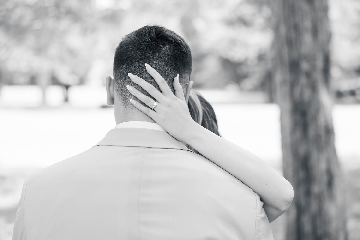 A black and white photograph showing a tender embrace between newlyweds in an outdoor setting.