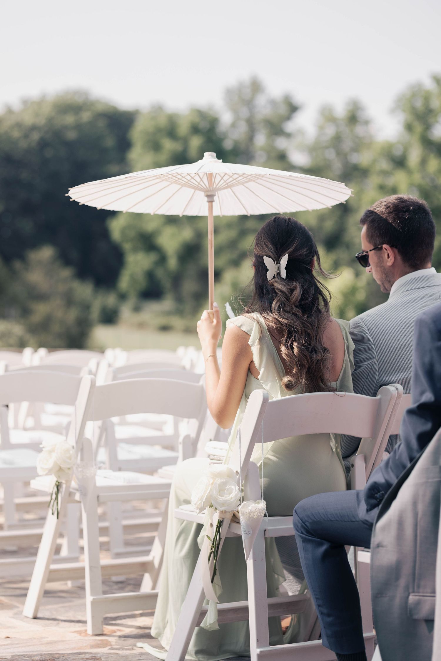 White parasols and chairs set up for outdoor wedding ceremony.