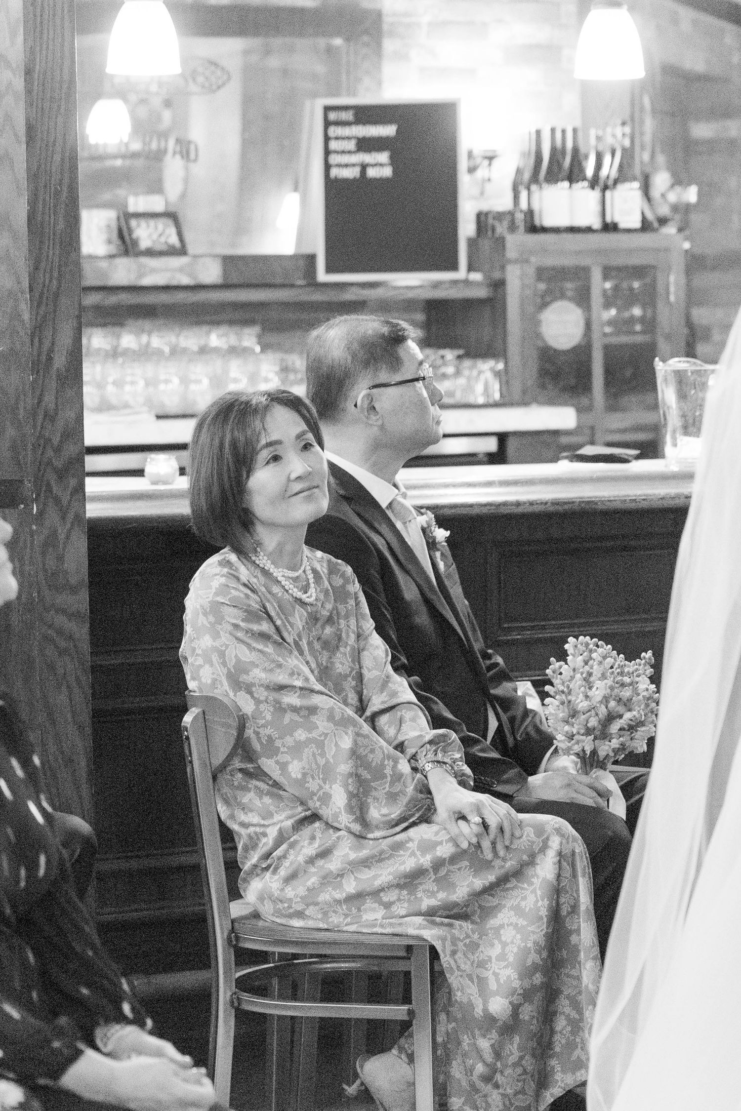 Woman in floral dress sits at a bar counter during a wedding reception.